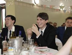 two men sitting at a table with wine bottles and silverware in front of them