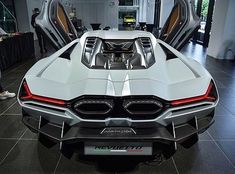 the rear end of a white sports car with its doors open in a showroom