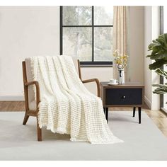 a white blanket sitting on top of a wooden chair next to a table with flowers