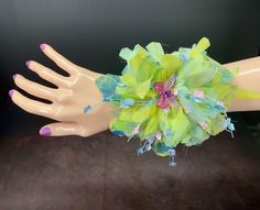 a mannequin's hand with green and pink flowers on it, holding onto a yellow wrist corsage