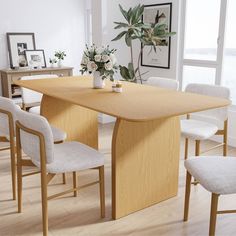 a dining room table with chairs and a vase on the end, in front of a window