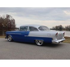 an old blue and silver car parked on the side of a road next to a body of water