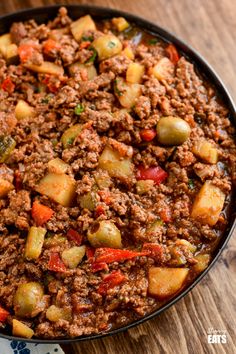 a pan filled with meat and vegetables on top of a wooden table