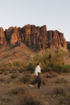 a man is walking through the desert with mountains in the background