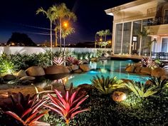 an outdoor swimming pool surrounded by plants and trees at night with palm trees in the background