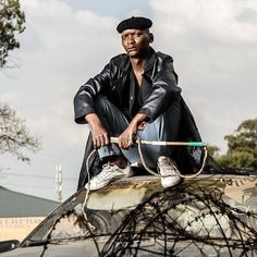 a man sitting on the hood of a car holding a broom and wearing a hat