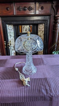 a glass cake stand sitting on top of a purple table cloth next to a fireplace