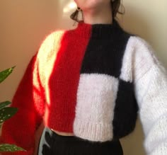 a woman standing next to a potted plant wearing a colorful sweater and black pants