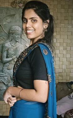 a woman in a blue sari is smiling at the camera and she has her hand on her hip