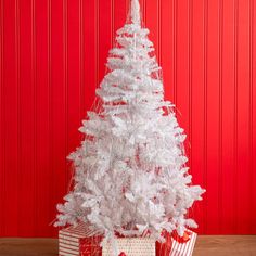 a white christmas tree sitting on top of a wooden table next to a red wall