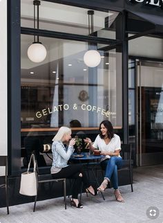 two women sitting at a table in front of a coffee shop