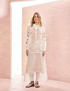 a woman standing in front of a pink wall wearing a white crochet dress