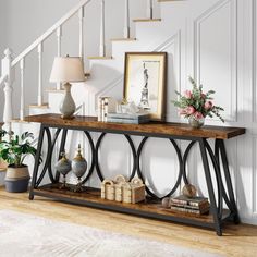 a console table with vases and flowers on it in front of a stair case