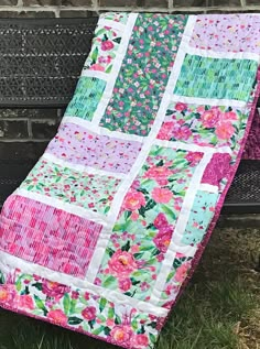 a pink and green patchwork quilt sitting on top of a bench next to a brick wall