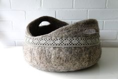 a gray felt basket sitting on top of a white table next to a brick wall