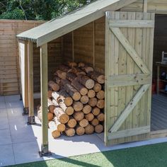 a pile of logs sitting inside of a wooden shed on top of grass covered ground