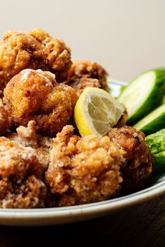 a white plate topped with fried food next to cucumbers and lemon wedges