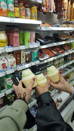 two people holding up cups in front of a store shelf filled with drinks and snacks