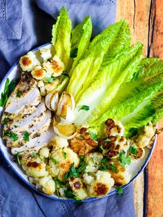 a bowl filled with chicken, cauliflower and lettuce on top of a wooden table