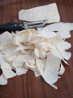 a pile of white paper sitting on top of a wooden table next to a knife