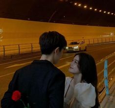 a man and woman standing next to each other in front of a highway at night