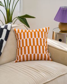 an orange and white pillow sitting on top of a couch next to a purple lamp