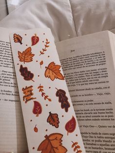 an open book with fall leaves on it next to a white pillow and some pillows