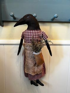 a black bird wearing a red and white checkered apron holding a potted plant