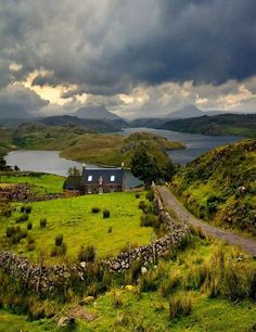 a house in the middle of a field with a lake and mountains in the background