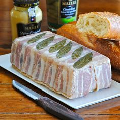 a piece of meat sitting on top of a white plate next to bread and knife