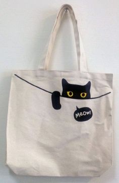 a white tote bag with a black cat drawn on it's front pocket