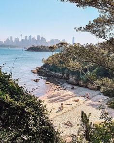 people are sitting on the beach near the water and in the distance is a city