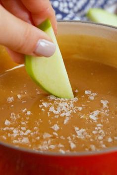 a person dipping an apple into a pot of soup