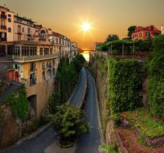 the sun is setting over an alley way in a small town with buildings on both sides