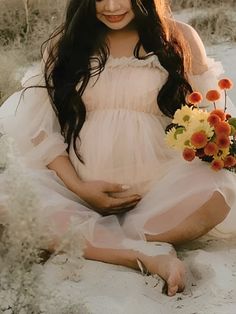 a pregnant woman sitting in the sand with flowers