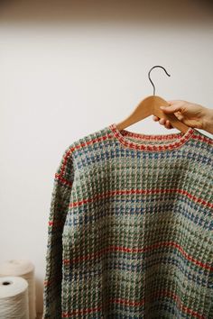 a person is holding up a sweater on a hanger next to two rolls of toilet paper