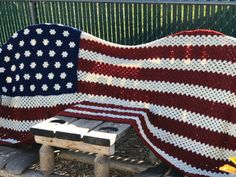 an american flag crocheted blanket sitting on top of a wooden bench next to a fence