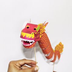 a hand holding a red paper dragon on a toothpick with its mouth open