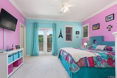 a bedroom with pink, blue and white walls has a television mounted on the wall