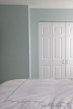 an empty bed with white sheets and two doors