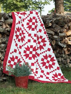 a red and white quilt sitting on top of a pile of wood next to a potted plant