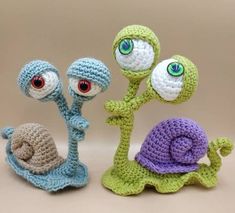 three crocheted toy snails and one snail with big eyes are standing next to each other