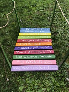 a set of seven colorful wooden signs sitting on top of a grass covered field next to a rope