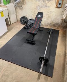 a gym mat with a bench and dumbbells on it in a basement area