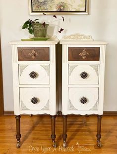 two white nightstands with drawers on top of them in front of a framed painting