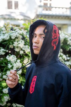 a young man with dreadlocks standing in front of trees Urban Hoodie With Embroidered Logo For Streetwear, Red Sweatshirt With Embroidered Graphics For Streetwear, Red Embroidered Sweatshirt For Streetwear, Urban Hooded Sweatshirt With Embroidered Logo, Black Hoodie With Embroidered Graphics For Streetwear, Black Embroidered Hooded Hoodie, Black Sweatshirt With Custom Embroidery For Streetwear, Black Custom Embroidery Sweatshirt For Streetwear, Black Custom Embroidered Sweatshirt For Streetwear