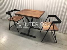 two wooden chairs sitting next to each other near a table and chair in front of a corrugated wall