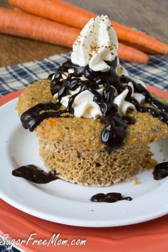 a carrot cake topped with whipped cream and chocolate sauce on a plate next to carrots