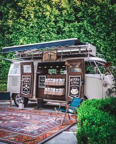 an old vw bus is parked in front of some bushes and trees with a coffee vending machine attached to the side