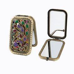 a small mirror with a peacock design on the front and side of it, sitting next to a compact case